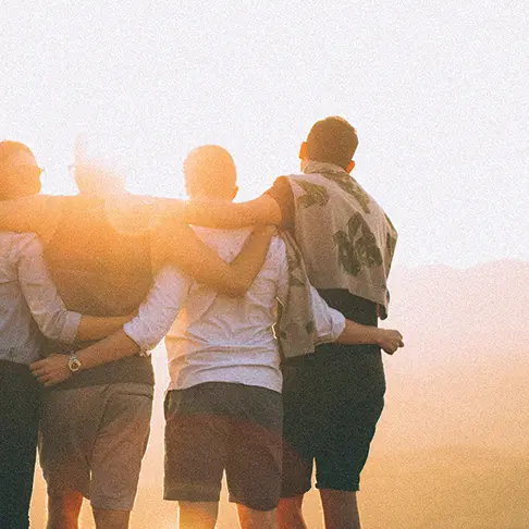 Menschengruppe blickt Arm in Arm in den Sonnenuntergang